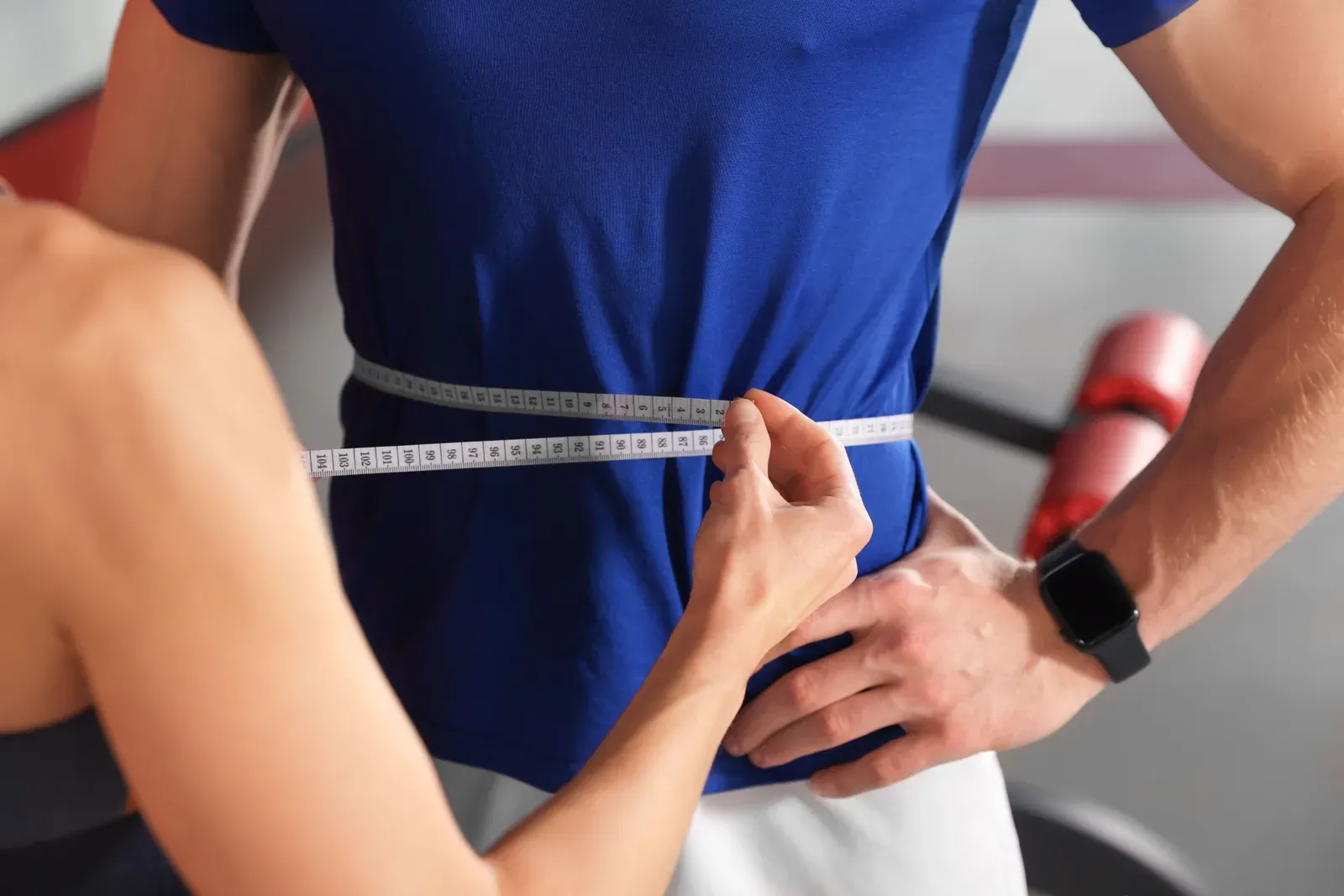 Coach measuring a client’s waist with a tape measure