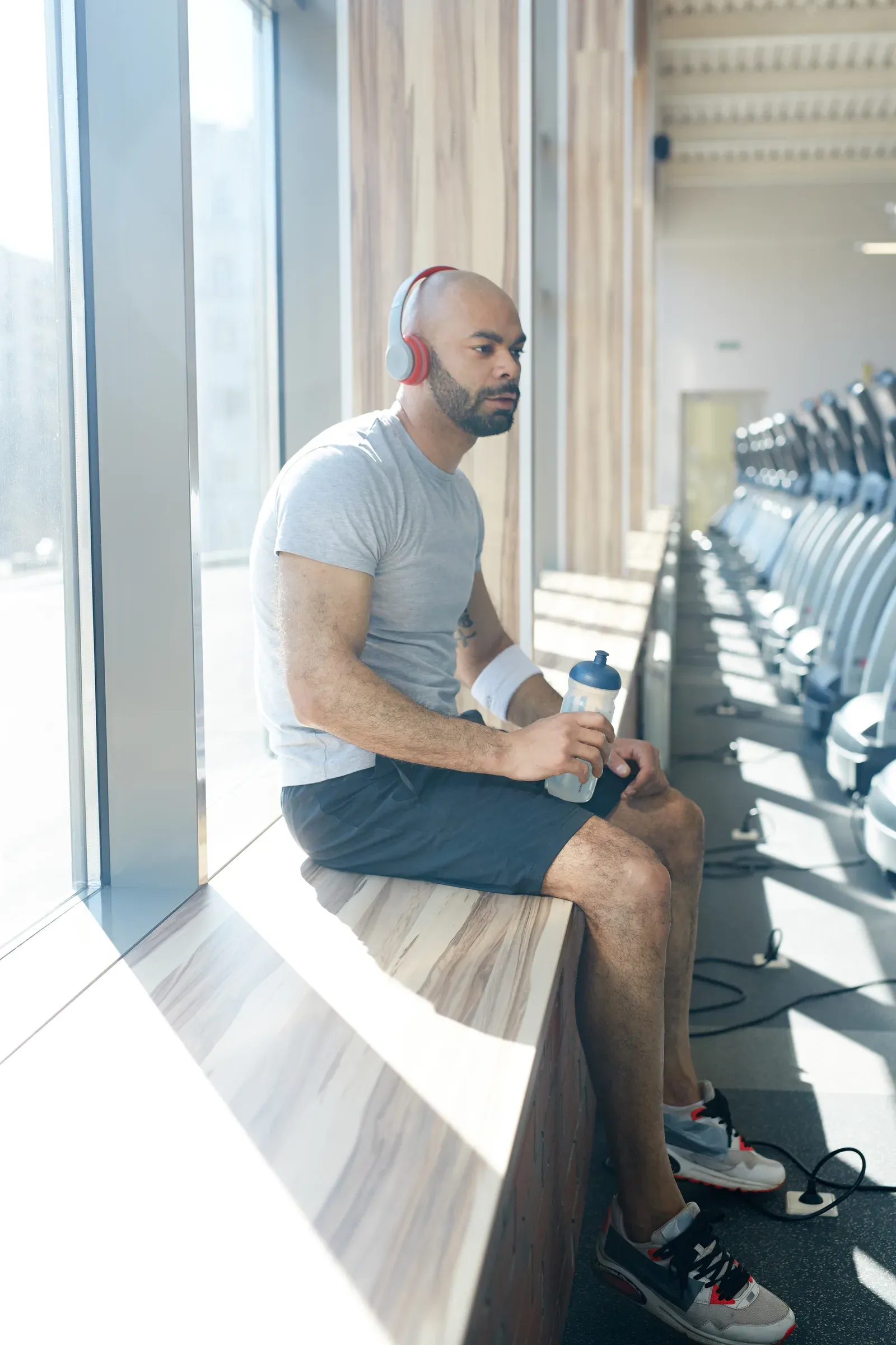 Man in his forties taking a breather on a gym window ledge between sets