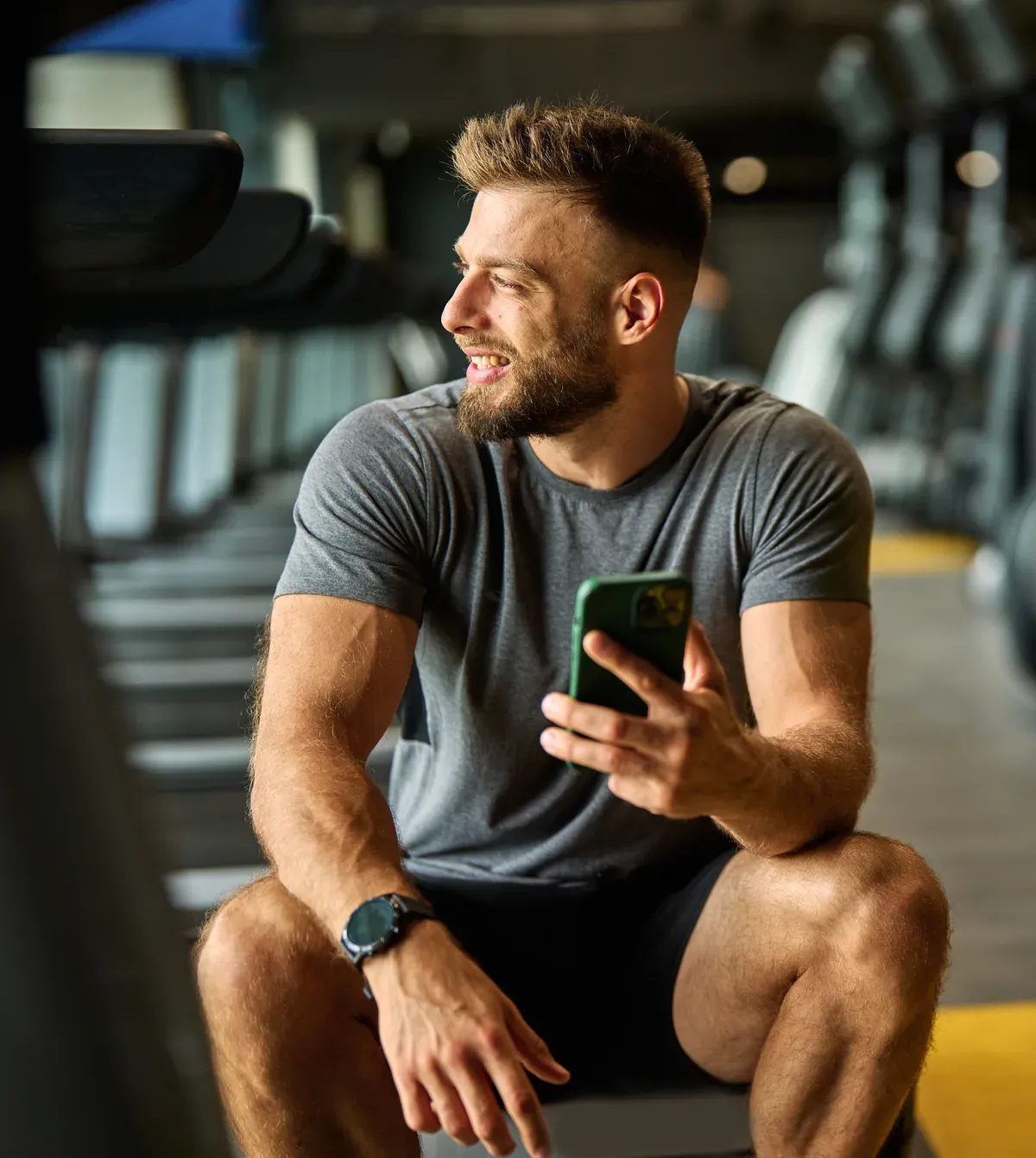 Man in a gym smiling at his phone between sets