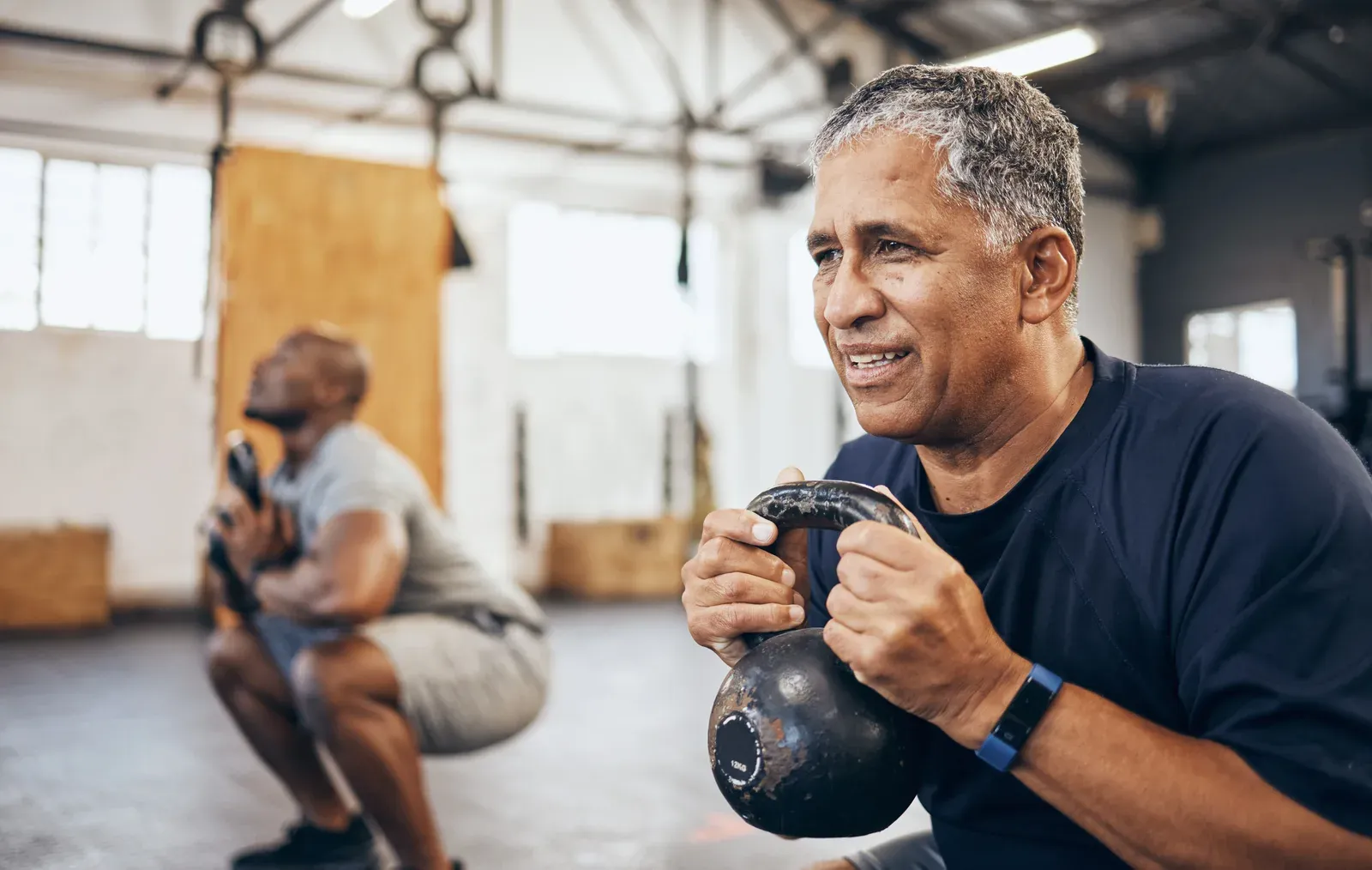 Coach guiding a mature man through a kettlebell exercise
