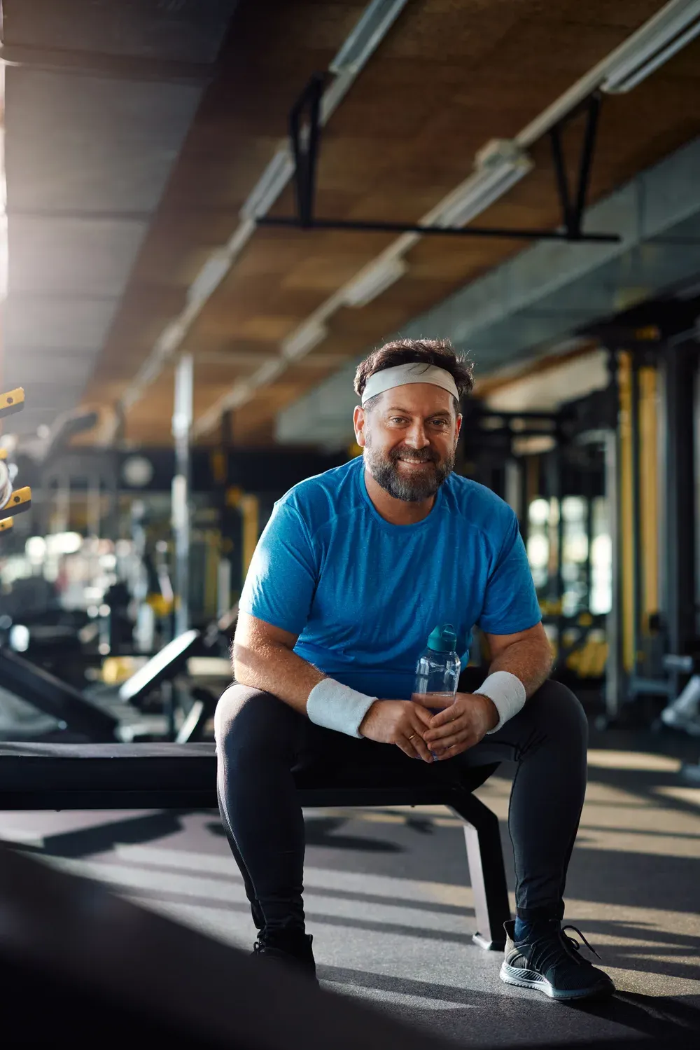 Man in his forties smiling on a gym bench with a water bottle