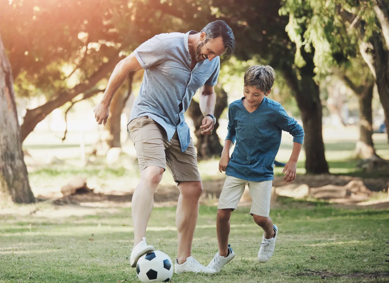 Father and son kicking a football around a park